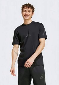 Musta urheilupaita, jossa on lyhyet hihat, pyöreä kaula-aukko ja hillityt logo-taidekoristeet. Kangas näyttää sileältä ja kevyeltä, sopien aktiiviseen käyttöön.