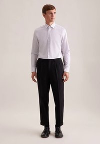 Camicia a righe bianche e grigie con bottoni, abbinata a pantaloni neri a pieghe. L'outfit è completato da scarpe nere lucide.