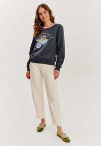 Tmavošedá mikina s grafickým motívom kvetinovej rukávky, smotanové nohavice a zelené baleríny s bielymi akcentmi. Textúrovaná tkanina a uvoľnený strih.