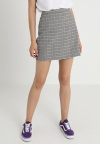 Mini gonna in bianco e nero a motivo houndstooth con vita aderente e forma a A, abbinata a sneakers viola. Tessuto piatto e liscio.