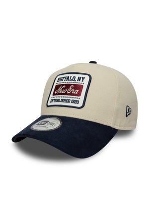 Beige cap with a navy blue brim. Features an embroidered logo patch with "Buffalo, NY" and "New Era" on the front. Adjustable fit.