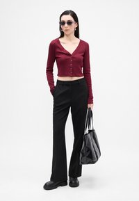 Cardigan scurt bordeaux cu nasturi, pantaloni negri adaptați, geantă mare neagră și pantofi masivi negri. Modelul poartă ochelari de soare închiși la culoare.