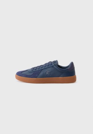 Navy blue sneaker featuring leather and suede materials, gum rubber sole, round toe, and lace-up closure with branding detail on the side.