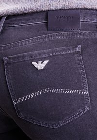 Ciemnoniebieskie dżinsy z logo w kolorze srebrnym na tylnej kieszeni, ozdobione rzędem małych cyrkonii nad szwem kieszeni.