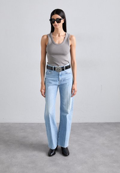 Canotta grigia a coste, jeans azzurri a gamba dritta a vita alta, cintura nera con fibbia argento, occhiali da sole neri, stivaletti neri.