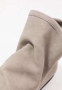 Stivaletto alla caviglia in suede grigio con una finitura morbida e testurizzata, caratterizzato da dettagli cuciti e un design sformato per un look rilassato.