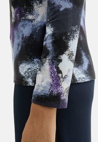 Triko s dlouhým rukávem s abstraktním potiskem v černé, fialové a modré barvě, vyrobené z měkkého materiálu s kulatým výstřihem a hladkým povrchem.