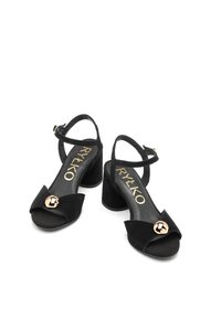Czarne zamszowe sandały na obcasie z otwartym palcem, skrzyżowanym paskiem na kostce oraz dekoracyjnym, okrągłym akcentem w różowym złocie na przodzie.