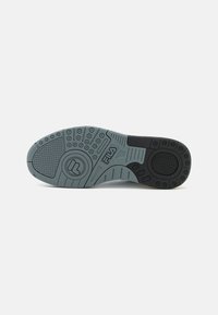 Suola di una sneaker, caratterizzata da una superficie in gomma grigia testurizzata con accenti neri, motivi circolari e un marchio impresso nel design.