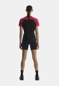 Krátký rukáv, černé a růžové sportovní oblečení s přiléhavým střihem, hladkou strukturou a malým logem na zadní straně.