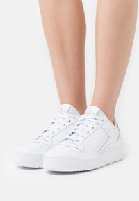 Vita sneakers med en slät läderöverkärna, perforerad tå, platta snörningar, vadderad krage och tjock sula med präglad logga.