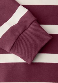 Poignet à manches longues sur un pull à rayures horizontales bordeaux et blanches, montrant une texture détaillée en tissu côtelé.