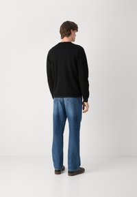 Czarna bluza z długim rękawem, luźny krój, ściągacze przy nadgarstkach, połączona z jasnoniebieskimi spodniami typu straight-leg i ciemnobrązowymi butami, widok z tyłu.