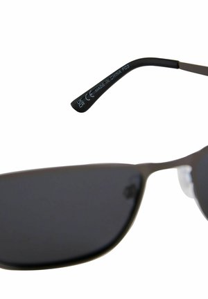 Occhiali da sole con lenti scure, montatura in metallo, design angolare e asta nera con un'etichetta bianca stampata che indica "Made in China."