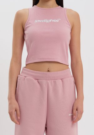 Frau trägt ein pinkes, geripptes Crop-Top mit "lowlights"-Logo und passende hoch taillierte Jogginghose, zeigt ihren Bauch und Bauchnabelpiercing.