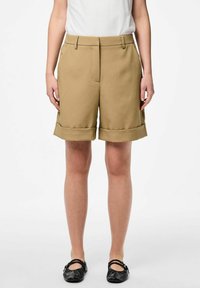 Khaki shorts met een tailored ontwerp, voorzien van een omslagzoom, zijzakken en een gladde textuur. Gecombineerd met zwarte platte schoenen.