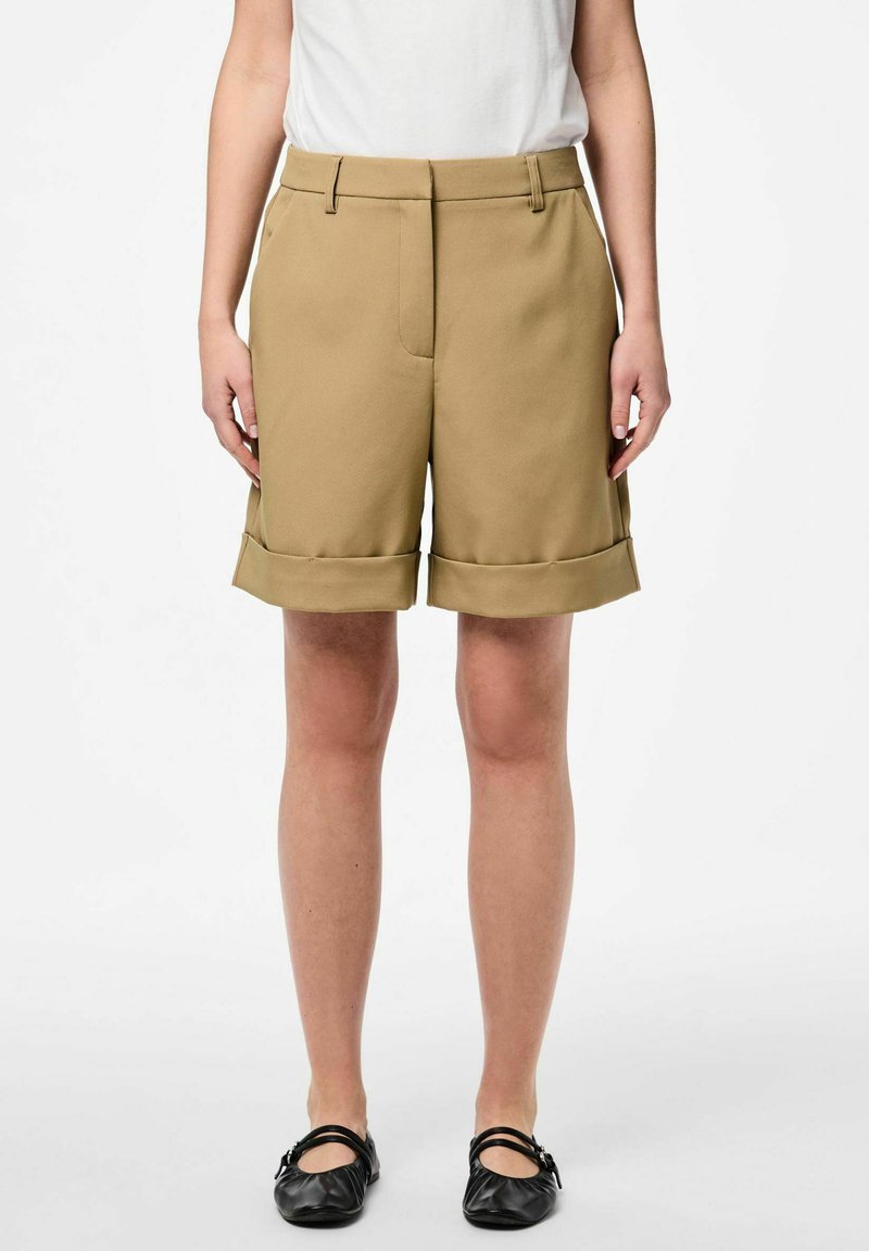 Khaki shorts met een tailored ontwerp, voorzien van een omslagzoom, zijzakken en een gladde textuur. Gecombineerd met zwarte platte schoenen.