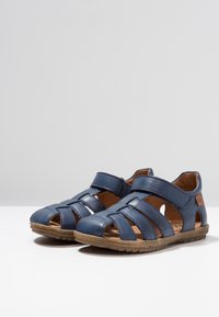 Námořnické modré kožené sandály s vyřezávaným designem, nastavitelným páskem a texturovanou gumovou podrážkou. Mají přirozený kožený interiér.