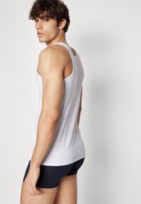 Débardeur blanc à la coupe ajustée, texture douce et encolure ronde, associé à un short bleu foncé, vu de côté.