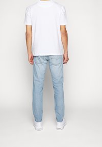 Vit bomull t-shirt och ljusblå jeans. Jeansen har bakfickor med sömnadsdetaljer. Skorna är vita sneakers.