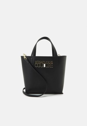 Czarna torebka typu tote z podwójnymi uchwytami, odpinanym paskiem na ramię oraz złotym logo "Versace Jeans Couture" z przodu.