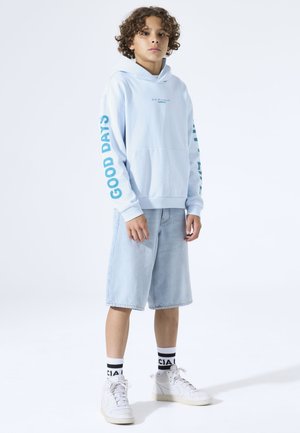 Lichtblauwe hoodie met de tekst "GOOD DAYS" op de mouwen, gecombineerd met lichte denim shorts en witte sneakers, met zwart-wit gestreepte sokken.