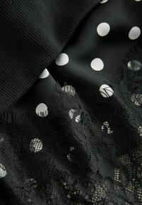 Black fabric layered with a polka dot pattern and intricate lace trim. Features ribbed texture at the top. Soft and lightweight materials.