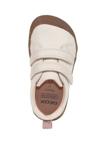 Zapato de cuero blanco con dos tiras de velcro ajustables, suela de goma marrón y un acento rosa en el talón. El interior cuenta con el logo de la marca.