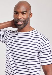 Camiseta blanca a rayas con líneas horizontales azul marino, material de algodón, cuello redondo, mangas cortas y pequeño logo de la marca en la manga.