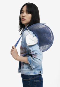 Blauer Mesh-Rucksack mit runder Form und strukturiertem Material, begleitet von einem silbernen herzförmigen Reißverschlussetui, das einzigartige Designdetails hervorhebt.