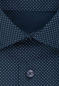 Granatowa koszula w białe kropki, z klasycznym kołnierzykiem, z przodu zapinana na guziki, o gładkiej bawełnianej fakturze.