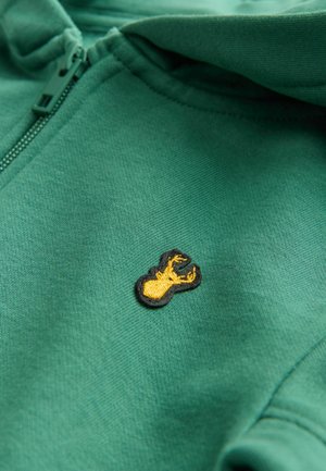Zelena zip-up dukserica napravljena od mekanog materijala, s žutim vezom u obliku jastoga na crnom obrubu. Glatka tekstura, standardan kroj.