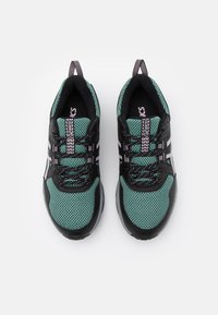 Chaussures de sport noires et bleu sarcelle avec dessus en mesh, accents blancs, semelle en caoutchouc texturée et lacets assortis, dotées d'une boucle à l'arrière pour un enfilage facile.