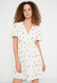 Φλοράλ φόρεμα σε λευκό ύφασμα, με κοντά μανίκια, βαθύ V-λαιμόκοψη και εφαρμοστή μέση με φούστα σε καμπάνα. Μικρά, πολύχρωμα λουλουδένια σχέδια.