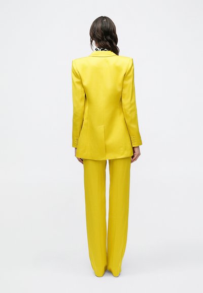Blazer giallo su misura e pantaloni a gamba larga. Tessuto liscio, design strutturato e maniche lunghe con dettagli a bottoni. Vista posteriore mostrata.