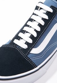 Baskets bleu marine et bleu clair avec lacets blancs et bande ondulée blanche sur le côté, vue rapprochée de l’avant et de la zone des lacets.