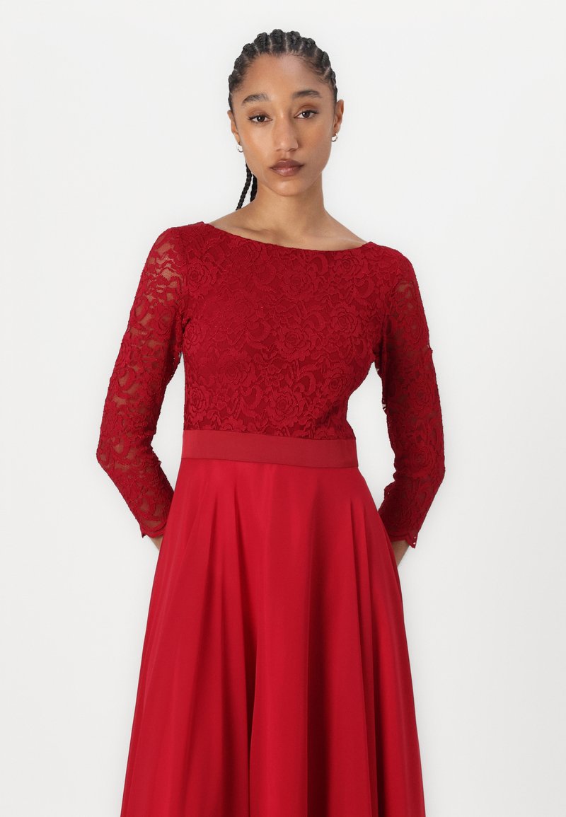 Rotes Spitzenkleid mit langen Ärmeln, tailliertem Oberteil und schwingendem Rock. Das Spitzenmuster zeigt florale Designs und sorgt für eine strukturierte Optik.