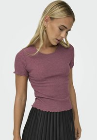 Hedvábný, krátký rukáv top v barvě mauve, s kulatým výstřihem a zvlněným lemem, doplněný plisovanou černou sukní.