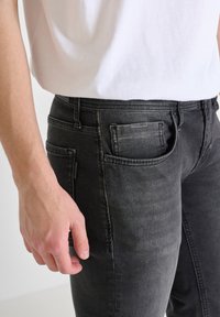 Jeans de mezclilla negra ajustados, con un diseño estándar de cinco bolsillos y un leve desgastado. Acompañados de una camiseta de algodón blanca.