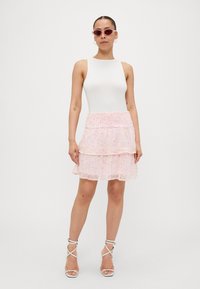Un body sans manches blanc associé à une jupe légère rose à volants avec un motif floral. Accessoirisé avec des lunettes de soleil roses et des talons blancs à lanières.