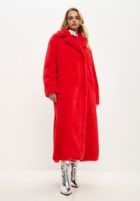 Abrigo largo de piel sintética roja con cuello, diseño de doble botonadura y bolsillos laterales; combinado con botas plateadas brillantes hasta la rodilla.