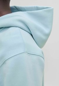 Sudadera con capucha azul claro que presenta una tela suave y texturizada, con una capucha grande y detalles de costuras visibles a lo largo de los hombros.