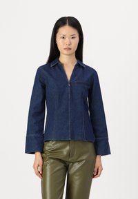 Mörkblå jeansjacka med dragkedja, spetsig krage och långa ärmar, med en framficka och kontrasterande söm.