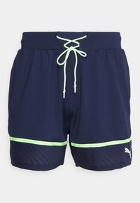 Navy blue urheilusortsit, joissa on neonvihreä naru ja raita helman lähellä, ja joissa on pieni valkoinen Puma-logo vasemmassa lahkeessa.