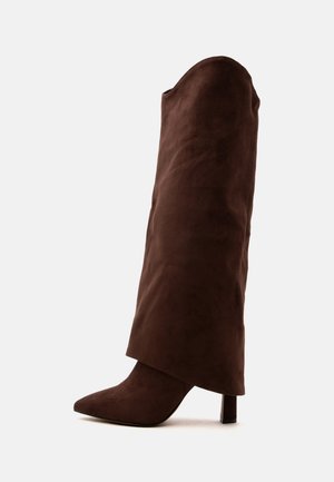 Botte haute en daim marron avec bout pointu et talon bloc sur fond blanc.