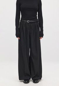 Black ribbed long-sleeve top paired with high-waisted black wide-leg trousers, featuring pleats and a black belt with a silver buckle.