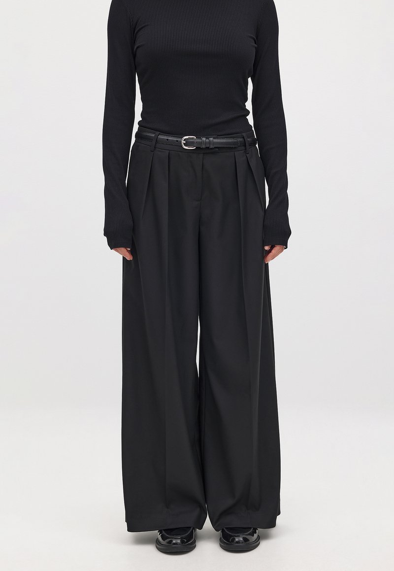 Black ribbed long-sleeve top paired with high-waisted black wide-leg trousers, featuring pleats and a black belt with a silver buckle.