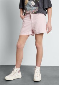 Ljust rosa linnebyxor med sidfickor och en avslappnad passform, i kombination med krämfärgade högklackade sneakers med guldöglor och ett logotypmärke.