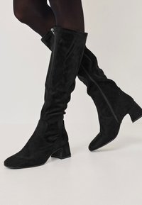 Black over-the-knee boots made of soft suede, featuring a pointed toe, block heel, and side zipper for easy wear, with a smooth texture.