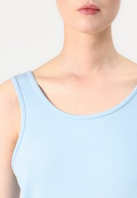 Svijetloplava majica bez rukava s okruglim izrezom i debelim naramenicama, izrađena od glatkog, rastezljivog materijala. Nema vidljivih uzoraka ili detalja.